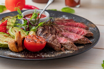 chopped medium rare steak with grilled vegetables. Sauce is served with the dish. Dish on a white plate in natural light.