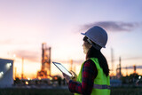 Fototapeta Paryż - Asian woman petrochemical engineer working at night with digital tablet Inside oil and gas refinery plant industry factory at night for inspector safety quality control..