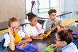 © LIGHTFIELD STUDIOS - schoolgirls talking while sitting in school eatery with multicultural classmates and teacher on background