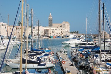 the port of Trani in Puglia with some some boats docked at the pier and the Cathedral in background in sunny summer day