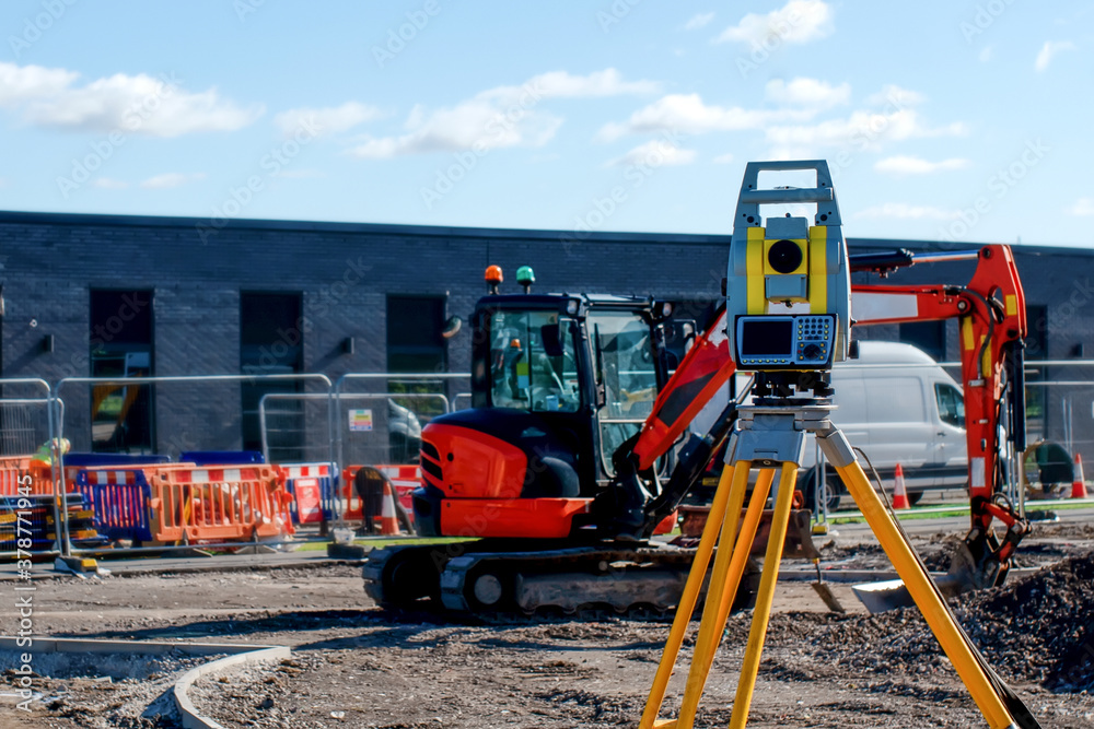 Yellow equipment set out on tripod on building site against cloudless blue sky. Construction site surveying engineering equipment, EDM, tacheometer set out on tripod site ready for setting out. - obrazy, fototapety, plakaty 