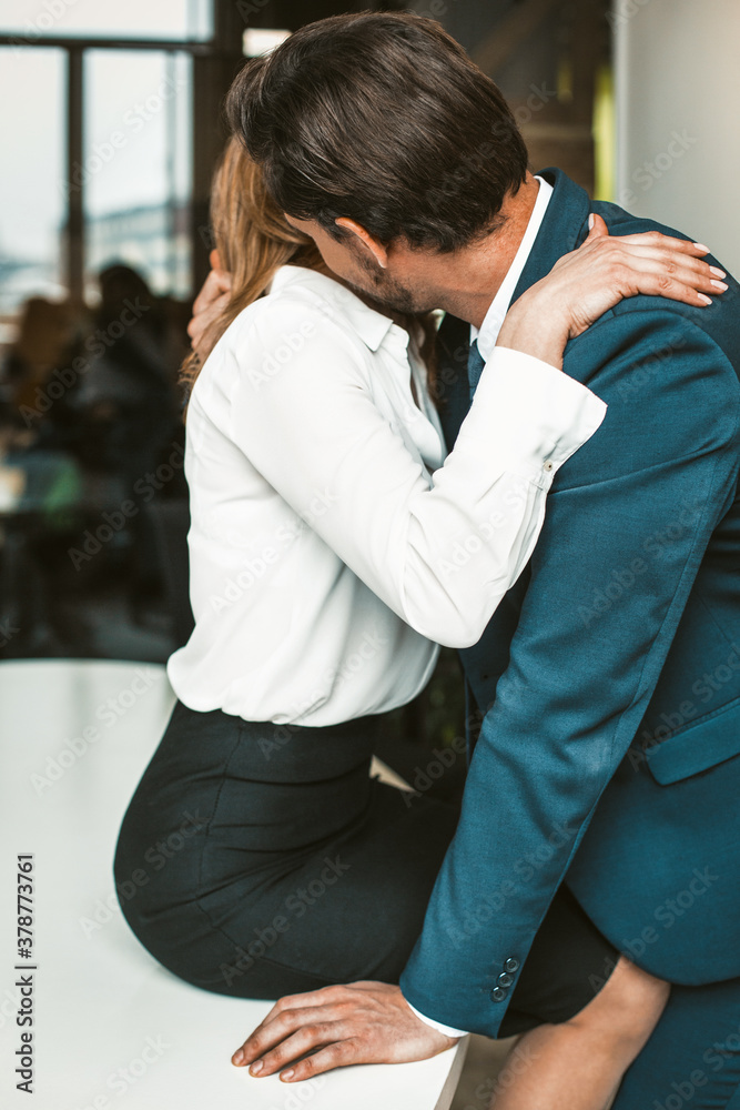 An Office Worker Sits On A Desk While A Colleague Kisses Her Neck an-office-worker-sits-on-a-desk-while-a-colleague-kisses-her-neck