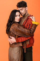 Wall Mural - trendy couple in leather jackets hugging isolated on orange