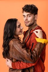 Wall Mural - young brunette woman hugging stylish man in jacket isolated on orange