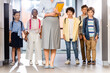 © LIGHTFIELD STUDIOS - cropped view of teacher with folders and notebooks near multicultural pupils in school corridor