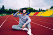 canvas print picture - Young caucasian male in active wear and headphones having break on training drinking water from bottle, thirsty sportsman in sound accessory making pause for refreshment on workout on stadium