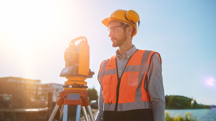 Wall Mural - Construction Worker Using Theodolite Surveying Optical Instrument for Measuring Angles in Horizontal and Vertical Planes on Construction Site. Worker in Hard Hat Making Projections for the Building.