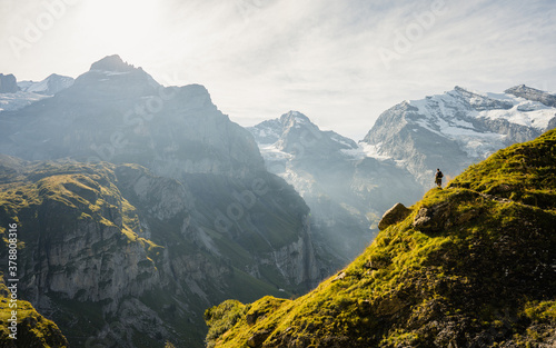 Cuadros en Lienzo An adventurous man stands on top of a mountain and enjoys a beautiful view during sunny summer day, Beautiful nature with steep mountains and rocks in background