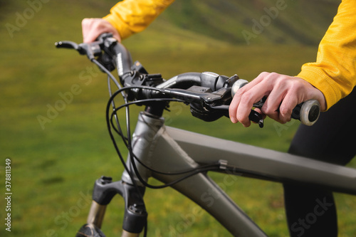 Close-up of female hands holding handlebars of mountain bike outdoors on green grass background