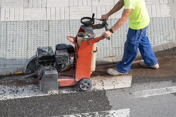 Construction worker cutting concrete floor with diamond saw blade machine on a sidewalk