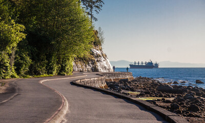 
Seawall and rock wall under overcast, the curved lines of the path around Stanley Park with its pine tree woods and the waters of the Pacific Ocean. Vancouver, British Columbia, Canada
