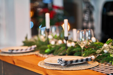 The festive Christmas table is decorated with branches of a Christmas tree, candles and garlands. Cozy home Christmas atmosphere.