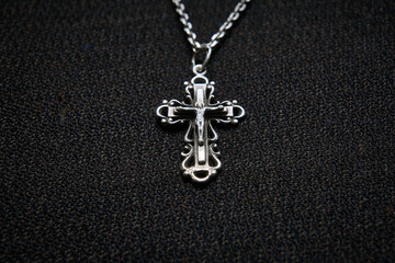 Cross on a silver chain, faith, spirituality and religion, dark fabric background.