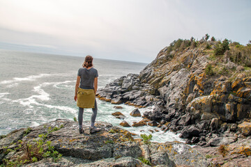 Sticker - Woman looking at a rocky coast by the edge of the ocean in summer