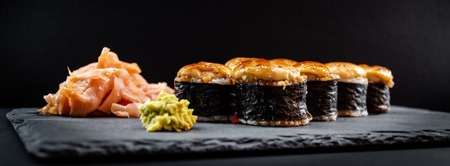 Wall Mural - Panoramic photo of served warm sushi rolled in nori sheets with ginger and wasabi on a black stone plate.