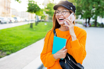 Lovely girl talking by mobile phone and smile.  Brunette long-haired  student walking after lessons in sunny park.