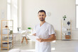 Smiling man doctor chiropractor or osteopath standing with notes and looking at camera
