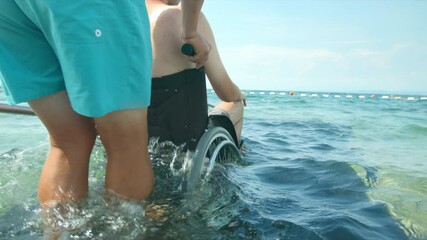 Wall Mural - Disabled man at beach going for a swim with help of a wheelchair and assistant.