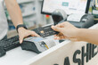 A hand of a customer is paying by contactless credit card with NFC technology. A seller with a credit card reader machine at the counter.  A female customer is holding a credit card. Focus on hand.