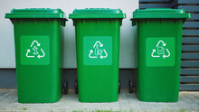 Green Colored, Plastic Garbage Bins, With Different Recycle Logos On Front, Stacked In Row Against Brown Wood Wall. Concept Of Waste Sorting For Food, Paper And Bottles. Saving Environment From Trash.