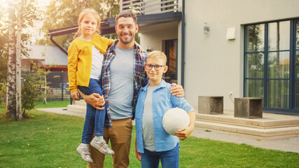 Portrait of a Happy Family of Three: Father, Daughter, Son. They Are Posing In Front of Camera on a Lawn Next to Their Country House and Smile. Dad is Holding the Girl in His Arms, Boy - Football.