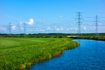 Landscape with river and meadows and power pylons
