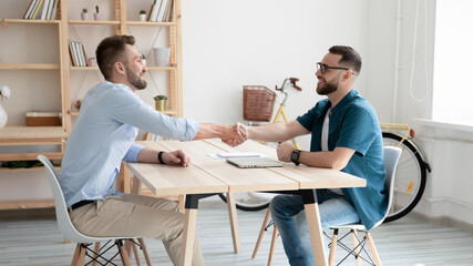 Wall Mural - Smiling hr manager wearing glasses shaking candidate hand on interview, greeting or congratulating, two business partners handshake, making agreement, signing contract, making successful deal