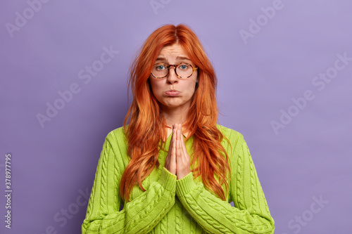 Cuadros en Lienzo Beautiful sad woman with pleading expression, keeps palms pressed together in pray and looks innocent at camera