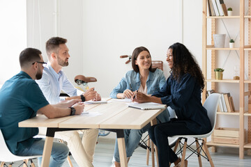 Diverse business partners discussing project strategy at meeting in modern office boardroom, smiling African American businesswoman speaking, sharing ideas with colleagues, group negotiations concept