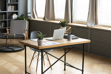 Modern empty wooden table with laptop and green plant on. Loft home workplace of freelancer or designer. Renovated stylish office workspace of businessman in apartment or flat. No people around.