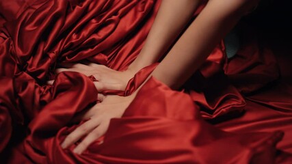 Wall Mural - Woman hands holding red satin sheet on bed. Unknown girl having moment pleasure.