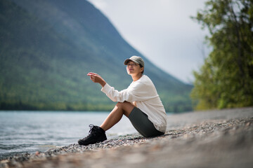 Young woman sit and relax on the mountain lake wearing sport clothes in Alaska trip