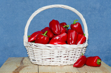 Wall Mural - Large white basket with ripe red paprika on a wooden table. Harvest paprika, bell peppers in a basket.