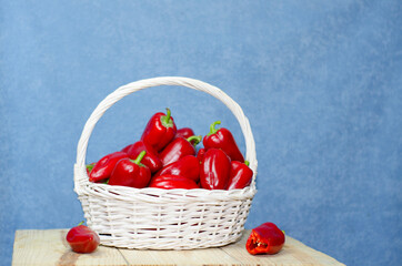 Wall Mural - Large white basket with ripe red paprika on a wooden table. Harvest paprika, bell peppers in a basket.