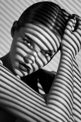 Black and white portrait of a beautiful woman with a shadow pattern on the face and body in the form of stripes.