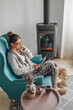 © perfectlab - woman by the fireplace, sitting in a cozy armchair, with a warm blanket and using tablet