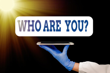 Wall Mural - Text sign showing Who Are Youquestion. Business photo showcasing inviting someone to join in your local group or company Displaying empty sticker paper accessories smartphone with medical gloves on