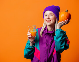 Pretty woman in 90s tracksuit with pumpkin juice on orange background