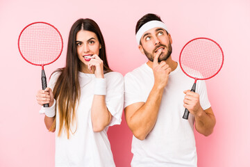 Wall Mural - Young couple playing badminton isolated relaxed thinking about something looking at a copy space.