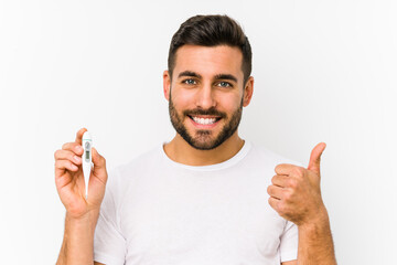 Wall Mural - Young caucasian man holding a thermometer isolated Young caucasian man holding  a smiling and raising thumb up