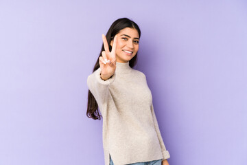 Wall Mural - Young indian woman isolated on purple background joyful and carefree showing a peace symbol with fingers.