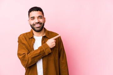 Wall Mural - Young latin man against a pink background isolated smiling and pointing aside, showing something at blank space.