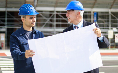 two architect developers reviewing building plans at construction site