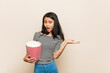 © Asier - Young asian girl holding a popcorn bucket impressed holding copy space on palm.
