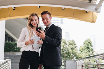 two businesspeople using a digital tablet and smartphone together in front of office