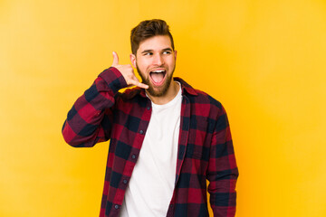 Wall Mural - Young caucasian man isolated on yellow background showing a mobile phone call gesture with fingers.