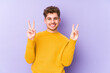 © Asier - Young blond curly hair caucasian man isolated joyful and carefree showing a peace symbol with fingers.