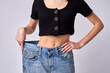 © DenisProduction.com - Slim girl shows off weight loss progress. Woman's stretching her old denim pants demonstrating her fitness achievement.