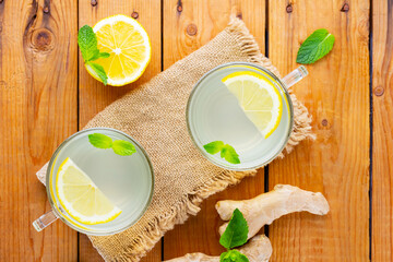 Wall Mural - Ginger tea with lemon on a burlap napkin. Two cups of ginger tea with mint on wooden background. Top view