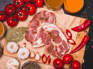 Raw beef steak with spices and cherry tomatoes on a dark slate, stone or concrete background. Top view with copy space